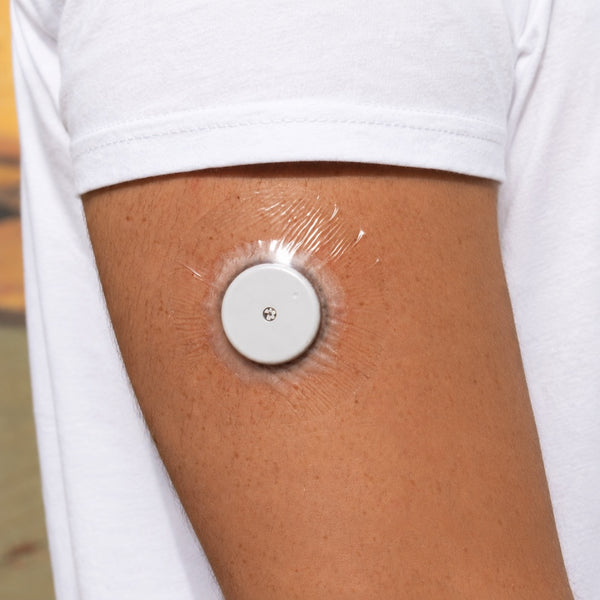 Parche Patch Me Up transparente sobre un sensor de glucosa blanco en el brazo